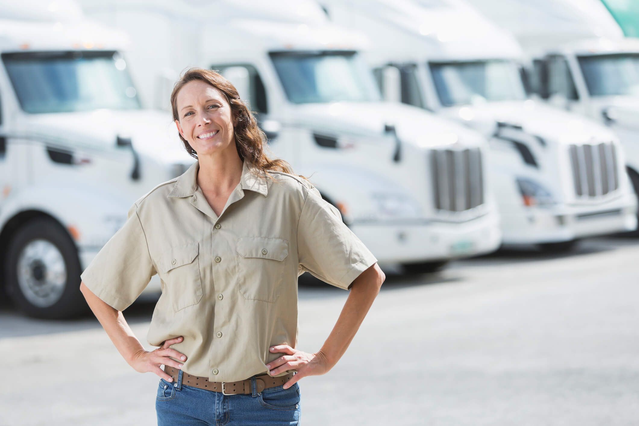 A fleet owner happily stands in front of her fleet of trucks.
