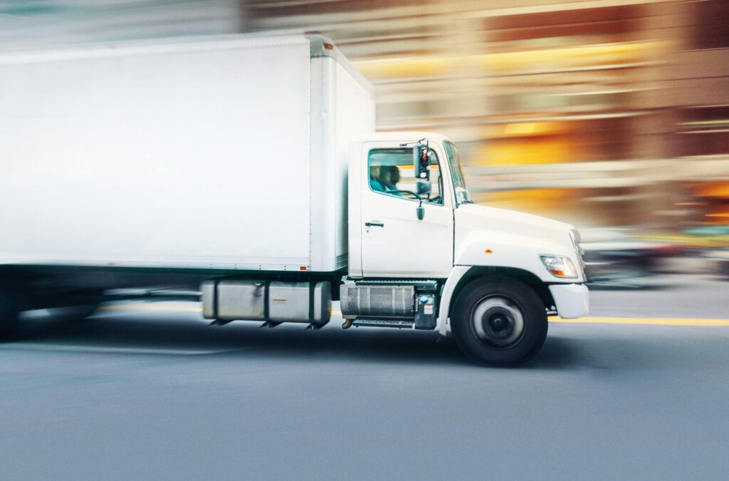 A delivery truck from a fleet whizzes down a busy city street.