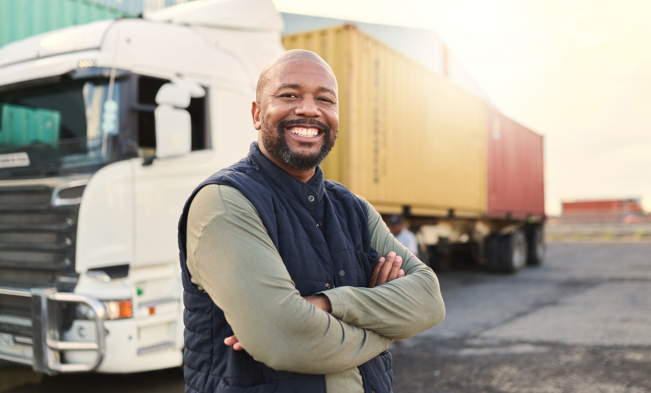 A happy fleet truck driver stands outside his semi truck.