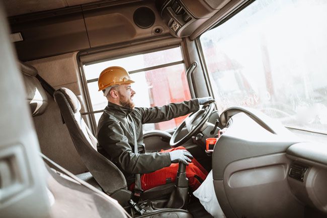 A truck driver in cab of truck driving down the road on his route.