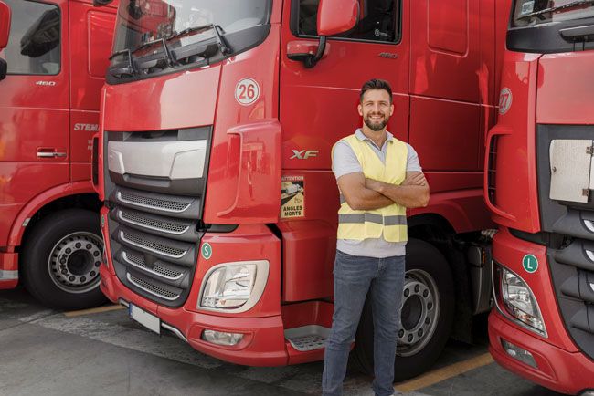 A truck driver stands in front of his fleet’s semi truck.